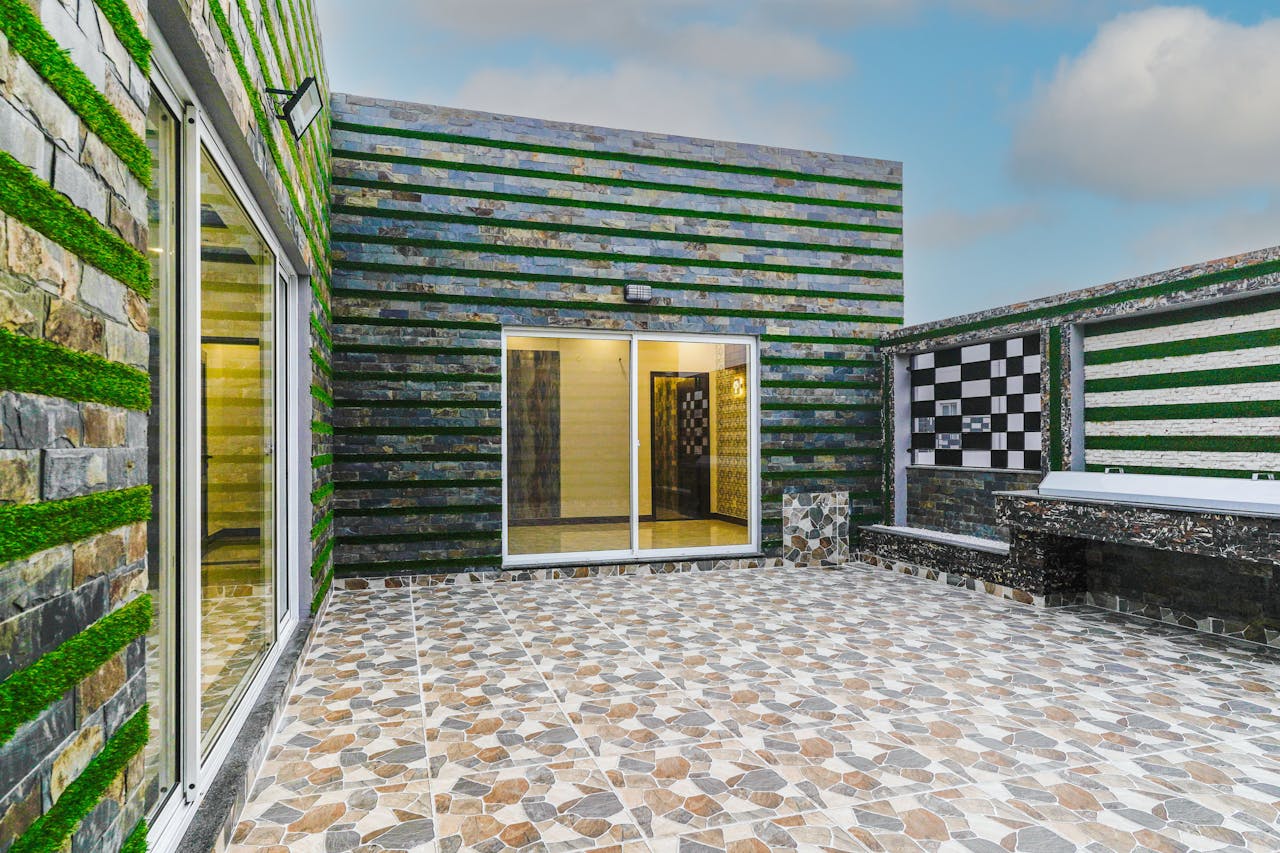 A contemporary outdoor patio featuring geometric tiles and green wall accents under a clear sky.